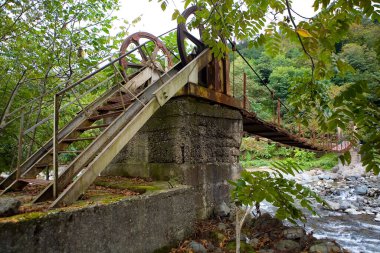 Dağ nehri üzerinde sıradışı, menteşeli bir köprü. Georgia.