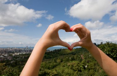 Kırmızı manikürlü kadın elleri Batumi 'nin arka planındaki kalp sembolünü gösteriyor. Georgia.