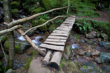 Kobuleti, Gürcistan, 10 Eylül 2018: Dağ nehri üzerinde küçük tahta bir köprü, insanlar diğer kıyıda bir masada oturuyorlar.