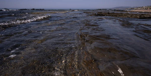 Sea waves crash against the coastal ridge of flat, beautiful rock formations on the shore.