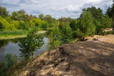 Dik, yüksek kumlu uçurum, çam ağaçları ve yemyeşil bir nehir kıvrımının üstünde.