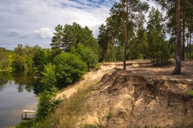 Dik, yüksek kumlu bir uçurum. Balıkçılık platformu ve yemyeşil bir nehir kıvrımı.