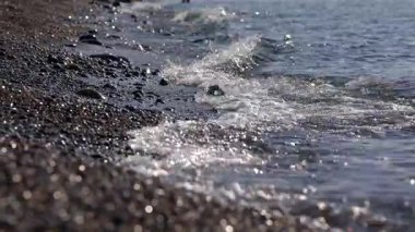 Köpüklü bir dalga, dalgaların huzurlu sesine doğru büyük çakıl taşlarının üzerinden süzülür..