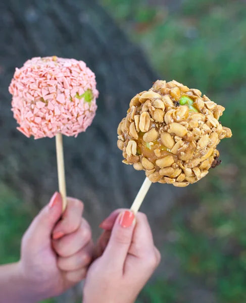 A woman hands holding candy apples with peanut butter, strawberry chocolate and peanuts on a wood background