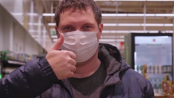 コロナウイルスの拡散からの保護。男は医療マスクを付け、承認に親指を上げる — ストック動画