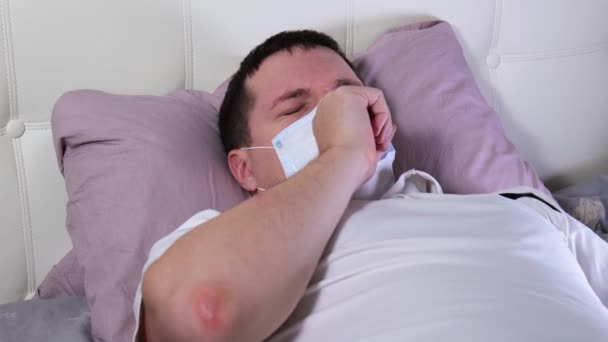 Белый мужчина, лежащий в постели, измеряет температуру. covid 19 — стоковое видео