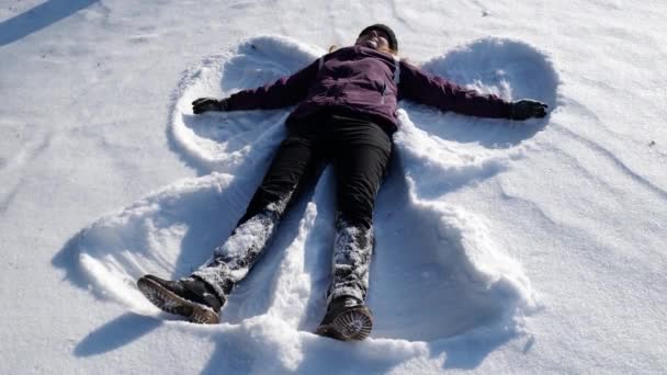 Ragazza fa un angelo di neve sdraiato nella neve. ragazza si rallegra nella neve — Video Stock