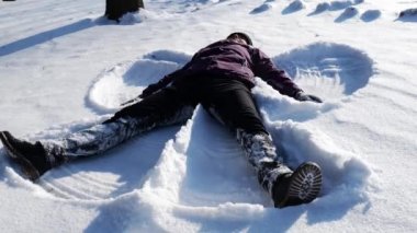 Kız karda yatan bir kar meleği yapıyor. Kız karda sevinir.