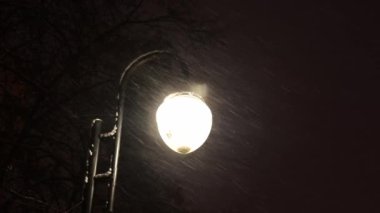 Bir sokak lambasının arkasına kar yağıyor.