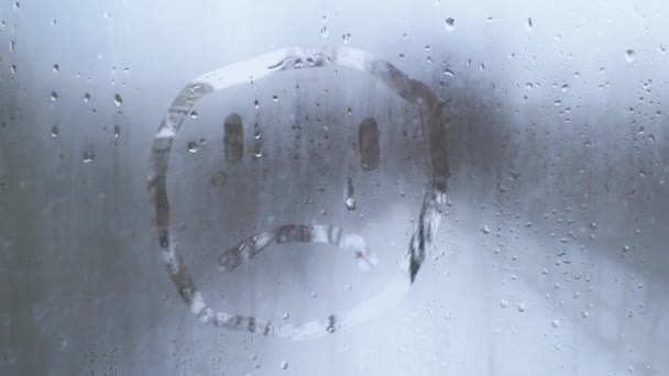 Hand malt ein trauriges Gesicht auf das vernebelte Glas. Symbol für Einsamkeit und Traurigkeit — Stockvideo