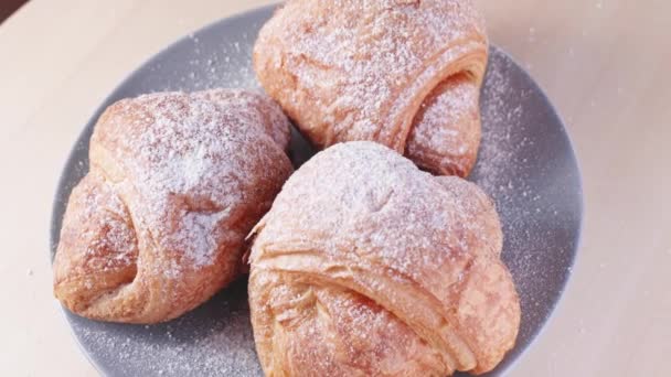 Frische Croissants mit Puderzucker auf einen Teller streuen. Langsame Rotation der Croissants — Stockvideo