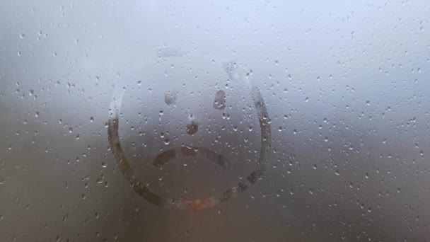 Drawing of a sad face on the fogged glass. a symbol of happy mood and sadness — Stock Video