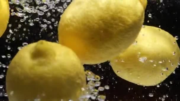 Lento mo limones cayendo en el agua sobre fondo negro — Vídeos de Stock