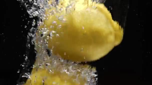 Повільні лимони падають у воду на чорному тлі — стокове відео