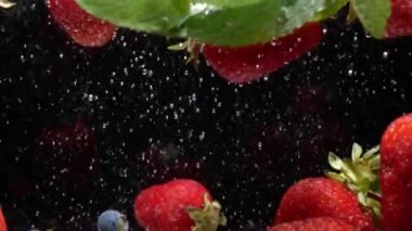 Yavaş hareket eden yaban mersinleri ve çilekler siyah arkaplanda suda