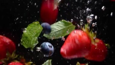 Yavaş hareket eden yabanmersini ve çilek damlaları siyah arkaplanda suya karışıyor.