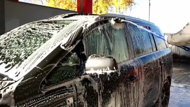 Araba yıkama servisinde arabayı yıkayan bir adamın dış yıkama işlemi sırasında köpükle kaplı bir fırçayla ıslak aracı elleriyle temizlemesine yakından bakın.. 