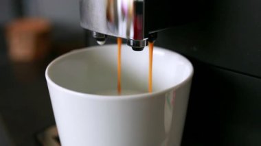 Kahve makinesinden bir fincana dökülen taze kahvenin yakın çekimi. Sıcak espresso demleme sırasında fincana akıyor. Kahve hazırlama kavramı, sabah rutini, kafein, kahve hazırlama süreci.