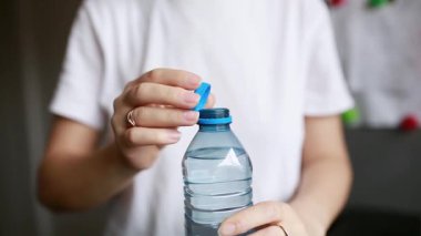 Genç bir kadının plastik bir şişeyi, mutfakta bağlı bir PET kapağıyla kapatırken yakın çekimi. El hareketine ve geri dönüşümlü nesne ile etkileşime odaklan, günlük ve çevreye duyarlı temalar için uygun.