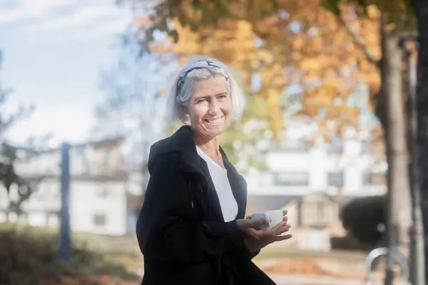笑顔の女性がコーヒーを飲みながら公園に座っている — ストック写真