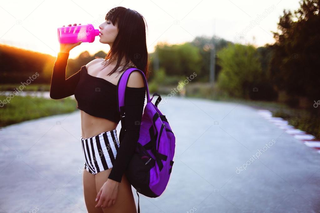 Athletic girl with protein shake and bag on the park after training relax .