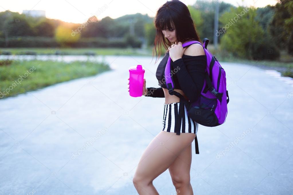 Athletic girl with protein shake and bag on the park after training relax .