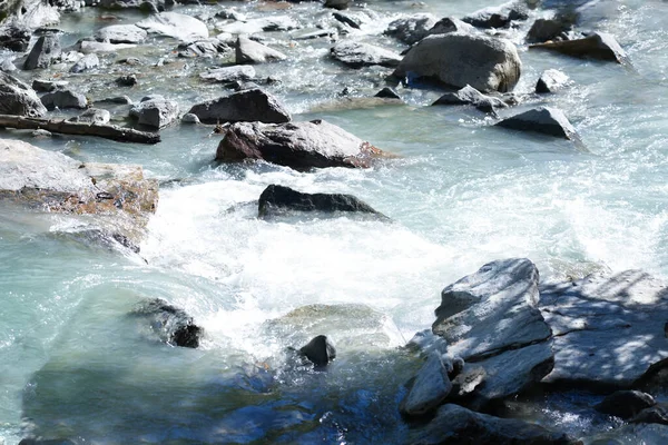 Nehir suyu kayaların üzerinde yavaşça akar. Güneş ışığının yüzeyde parladığı huzurlu bir sahne yaratır. Doğanın güzelliğini ve sakinleştiren etkilerini gösterir.