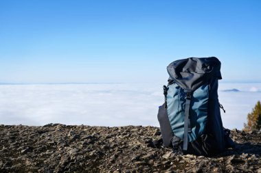 Açık mavi gökyüzüne karşı kayalık bir çıkıntıda duran sırt çantasıyla manzaralı dağ manzarası