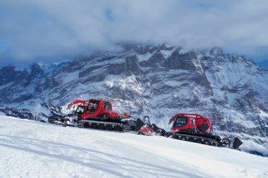 Kar tımarcıları İsviçre Alplerinde karlı bir yamaçta, yüksek dağ zirveleri ve dramatik bulutlu gökyüzü ile çevrili.