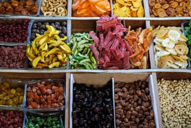 Yerel bir markette ahşap tepsilerde sergilenen çeşitli kurutulmuş meyve ve fındıklar, zengin renkler ve yiyecek maddelerinin dokularını ön plana çıkarıyor.