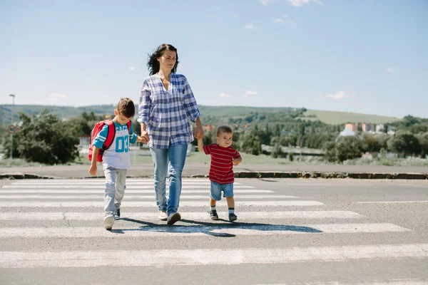 Mor och hennes barn som korsar vägen på väg till skolan. — Stockfoto