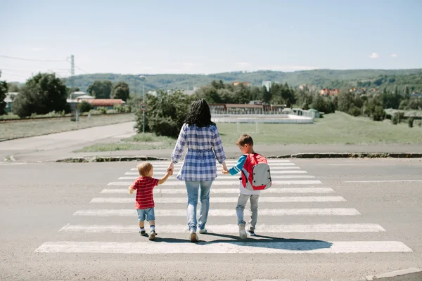Mor och hennes barn som korsar vägen på väg till skolan. — Stockfoto