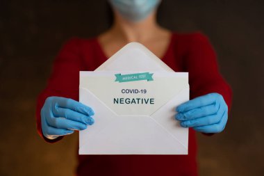 Covid-19 için kadın Negatif Antijen Algılama Testi. Yüz maskesi takan tanımlanamayan kişi ve mavi cerrahi eldivenler kameraya hızlı tıbbi testin negatif sonucuyla açık zarfı gösteriyor..