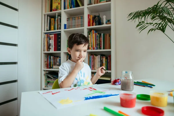 絵を考える口の上に指でかわいい子供 未就学児は彼の左の手で絵筆でインスピレーションを得る ストックフォト