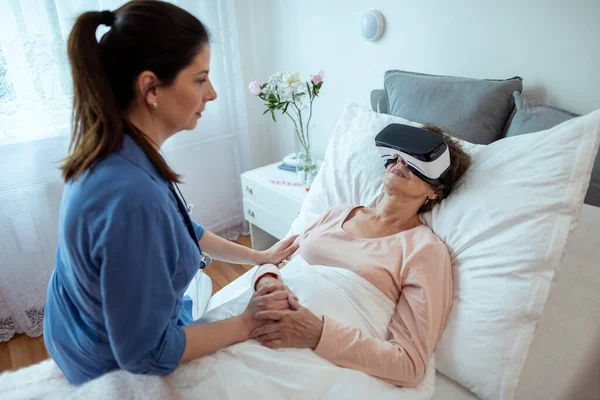 Sanal gerçeklik kulaklığıyla hastanede dinlenen yaşlı kadın hasta. Ev Hemşiresi Yatağında Oturan Yaşlı Kadın Via VR Teknolojisi ile Tedavi Ediliyor.