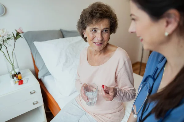 Ältere Frau Mit Roter Pille Der Hand Diskutiert Mit Pflegerin Stockbild