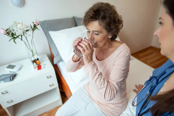 Seniorin Trinkt Wasser Ältere Patientin Sitzt Mit Krankenschwester Auf Krankenhausbett Stockbild