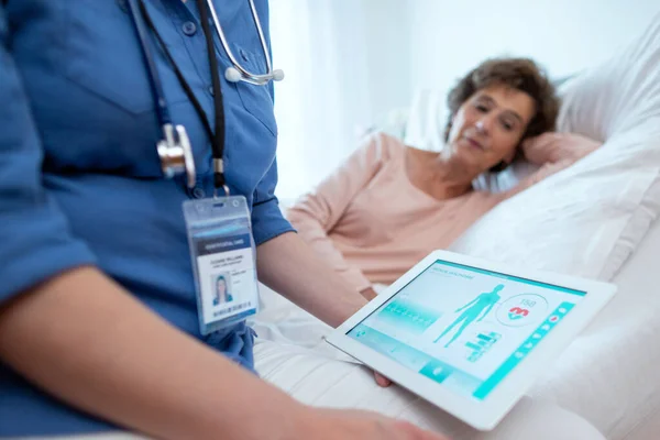 背景にベッドに横たわっ高齢女性患者のテスト結果を示すデジタルタブレット 医療記録を表示する医療用ソフトウェアアプリケーションとデジタルタブレットの閉鎖 ロイヤリティフリーのストック画像