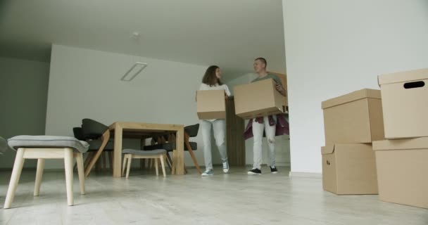 若い夫婦が箱付きのアパートに到着した 新しい家に段ボール箱を運ぶ20代の男性と女性 スローモーション 手持ち撮影 ワイドショット — ストック動画