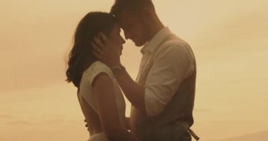 Erkek erkeğe öpüşen bir çift. Nazik damat, gelinin yüzüne dokunarak gün ışığında dokunuyor. Gerçek zamanlı, el kameralı, yakın çekim, 4K.