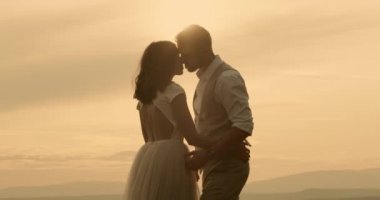 Bride and groom kissing in sunlight. Bride and groom holding hands and kissing face to face in sunlit countryside. Real-time, hand-held shot, medium shot, 4K.