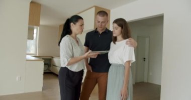 Yeni dairede dijital tablet kullanan emlakçı genç çifti gösteriyor. El yapımı, orta boy, 4K..