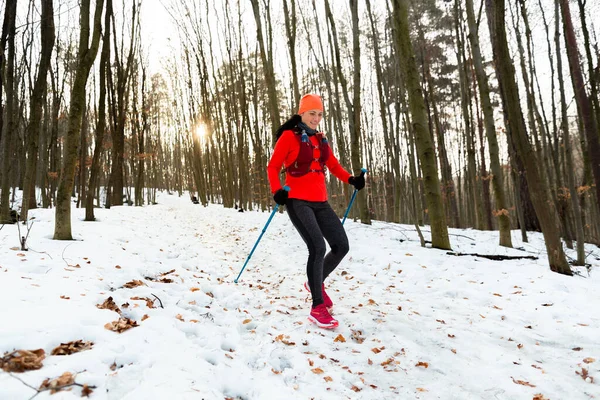 冬に走る女トレイル 寒い冬の日にトレッキングポールで丘を走っている笑顔の女性ランナー ロイヤリティフリーのストック画像