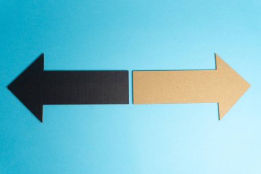 Kağıttan yapılmış iki ok açık mavi bir yüzeye oturur. Bir ok solu gösterir ve siyahtır, diğeri ise sağı gösterir ve bronzlaşır. Bu bir karar anı..