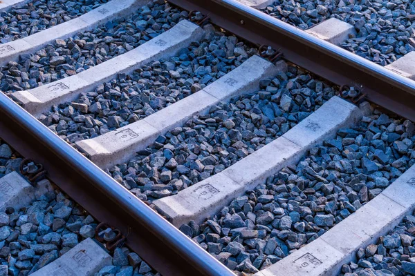 Paralel demiryolu raylarının yakın çekim görüntülerine göre beton yatakları ezilmiş taş safrasında eşit olarak duruyor. Metal raylar bağlayıcı şarjörlerle uyuyanlara bağlanmış. Yinelenen uyuyanların ve taşların şekli yapıyı ve stabi 'yi vurguluyor.