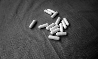 Masanın üzerinde çeşitli sarı, beyaz haplar ve tabletler var. Bazıları su toplamış, bazıları açılmıştı. Karışık ilaç kapsülleri ve tabletlerinin yakın çekimi, kısmen kullanılmış haplar, sağlık hizmeti, tedavi veya eczane konsepti ile açılan ambalaj.