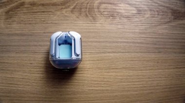 Beyaz kablosuz Bluetooth kulaklıklar ahşap masada şarj ediliyor. Modern cihaz, akıllı telefon ve müzik için taşınabilir ses aygıtı, minimalist teknoloji natürmort yaşam konsepti.
