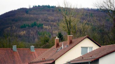 Kırmızı kil kiremitli çatılar ve tuğla duvarlı ön cepheli evler ve görünür bacalar. Avrupa 'da geleneksel konut binaları, mavi gökyüzünün altında fayanslı kiremitli çatılar ve taş duvarlar, samimi şehir manzarası.