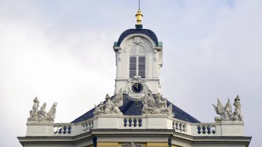 Her iki tarafında büyük beyaz saat yüzleri olan uzun taş saat kulesi belirgin bir şekilde yükseliyor. Gotik mimari ayrıntıları zaman arkaplanını temiz bir gökyüzü arkaplanına karşı çerçeveler. Yapı, eski bir Avrupa kasabasının simgesi olarak duruyor.,