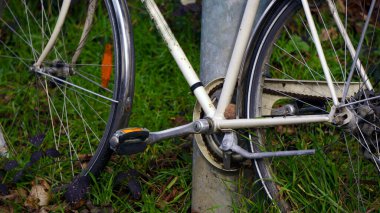 Eski bir bisiklet dışarıda dikey bir metal direğin ya da borunun yanında duruyor. Çerçeve yıpranmış, paslı detaylar ve solmuş boya yaşını ve uzun süre kullanıldığını gösteriyor. Yumuşak doğal ışık metalin dokusunu vurgular ve nostaljik bir hava yaratır.,